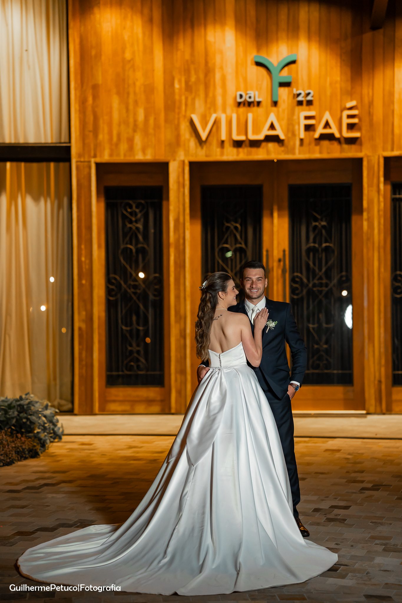 Casal de noivos em frente à entrada da Villa Faé com a logo iluminada